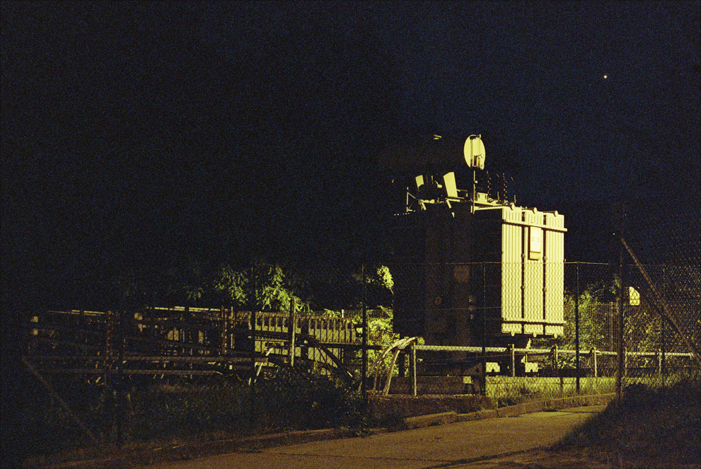 A large electric transformator illuminated by a single street lamp.  Shot on Cinestille 800T.