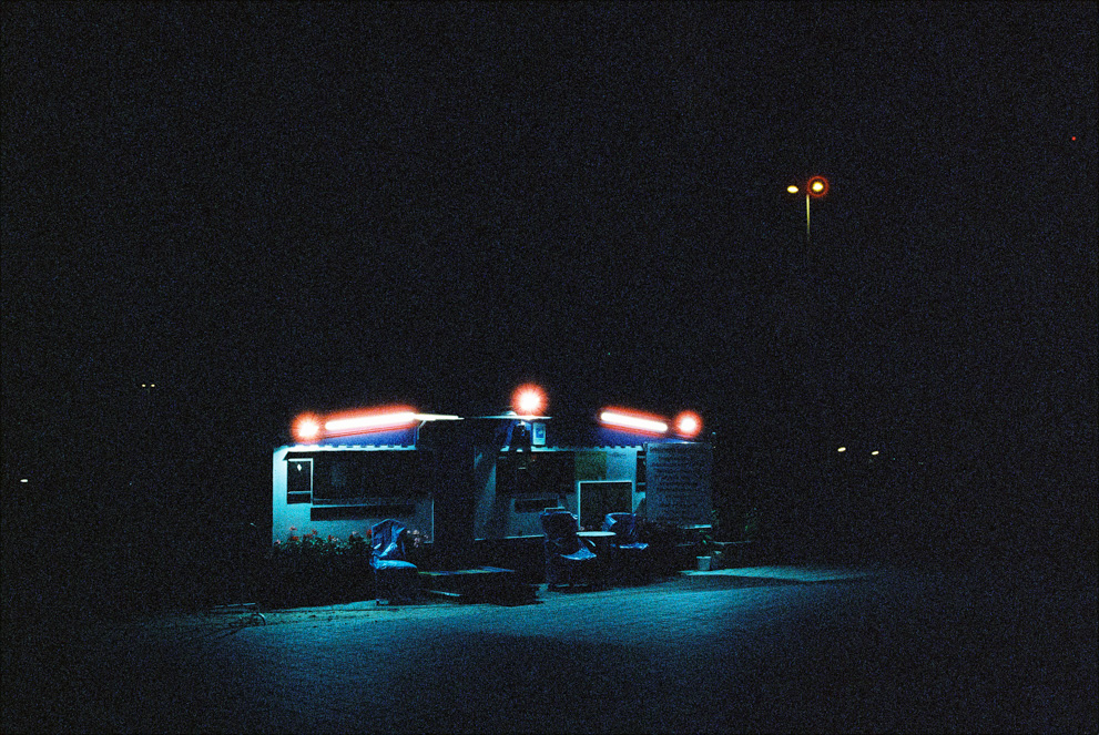 A camper with bright lights on a dark parking deck. Shot on Cinestille 800T.