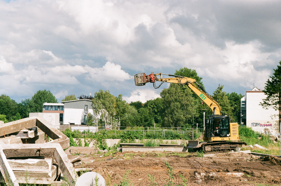 An escavator tearing down an old building with impressive clouds on the background. Shot on Fujifilm Fujicolor C200.