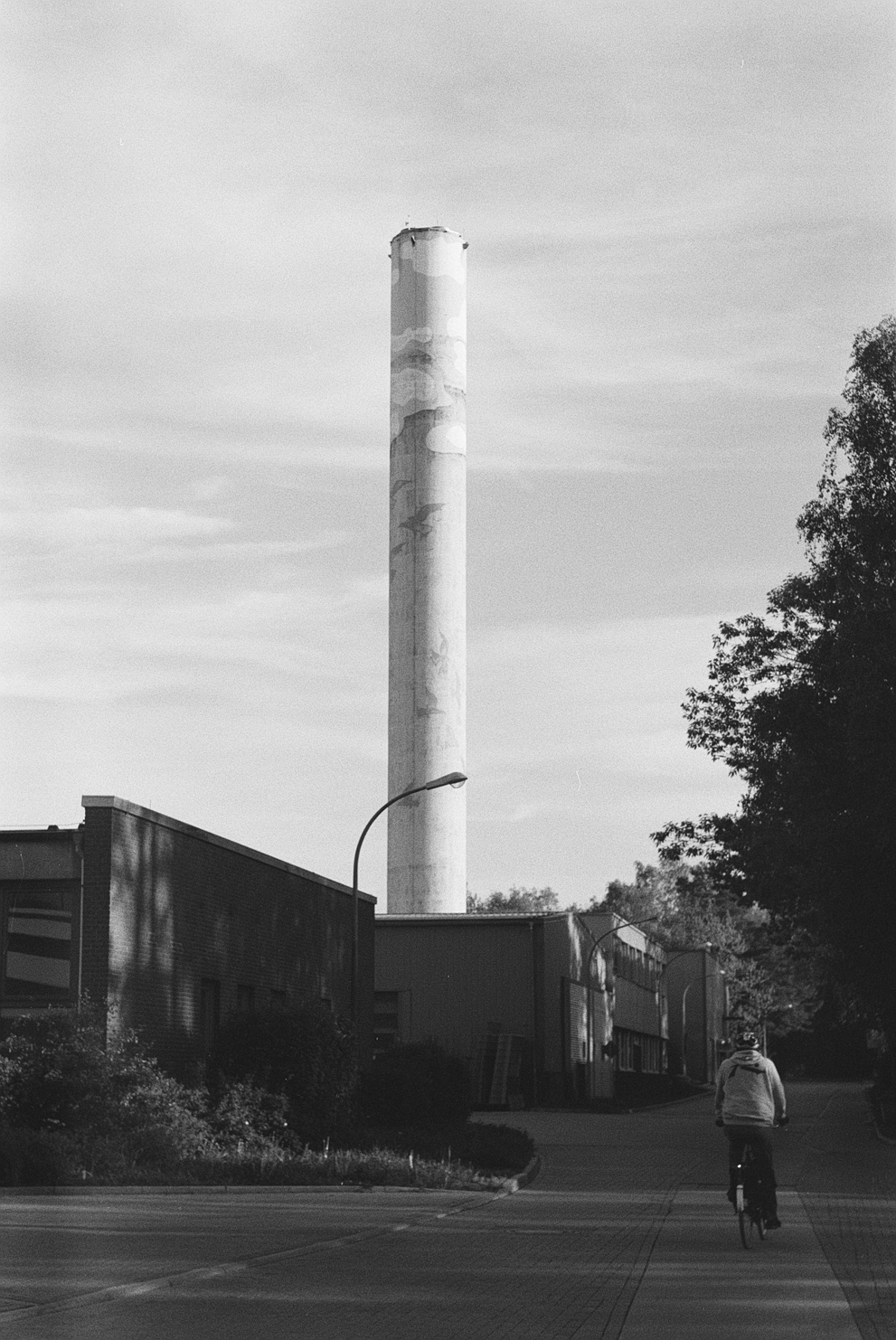 A person cycling down the road with a large chimney. Shot in Ilford Delta 400