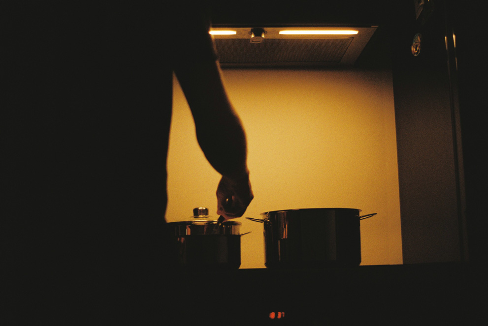 Dinnertime. The silhouette of a cook against the tungsten lights of his kitchen stove. Shot on Kodak ColorPlus 200.